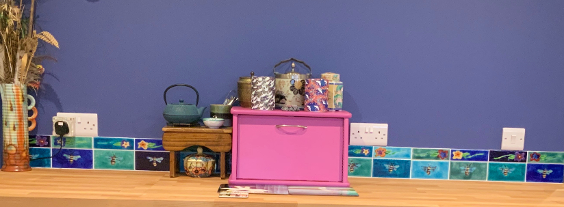 Hand-painted bespoke ceramic tiles by Noreen Jaafar installed in a customer’s kitchen, featuring colourful floral and bee motifs along a custom splashback